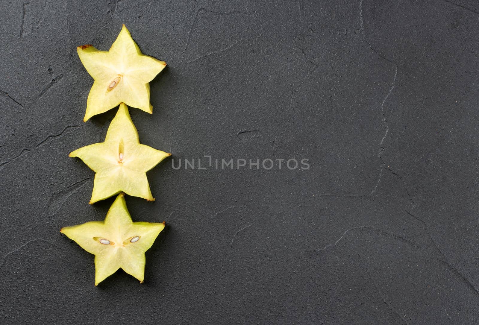 Three juicy slices of carambola fruit on a dark background, top view