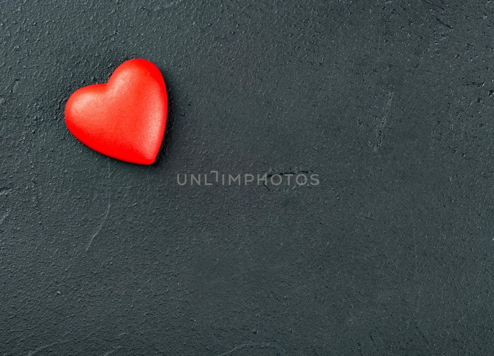 One red plastic heart on an empty concrete background, top view