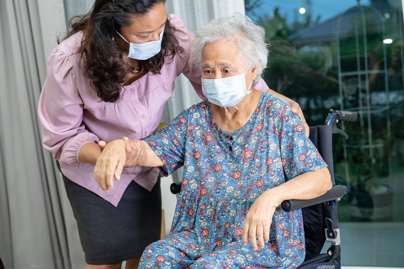 Caregiver help Asian senior or elderly old lady woman sitting on wheelchair and wearing a face mask for protect safety infection Covid 19 Coronavirus. by pamai