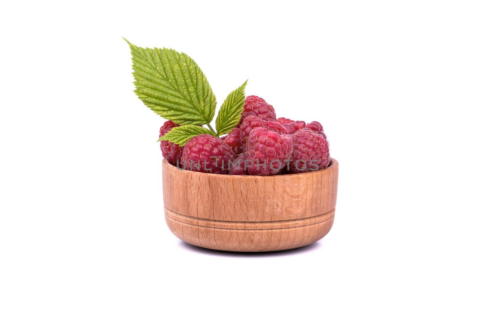 Full wooden bowl of fresh raspberries with leaves on a white background