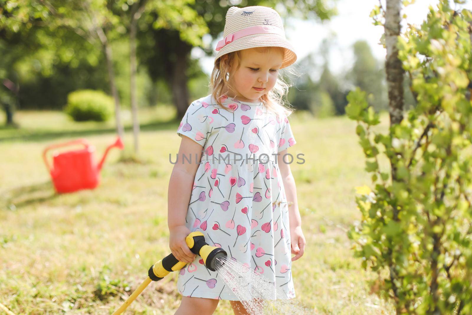 Adorable little girl playing with a garden hose on hot sunny summer day