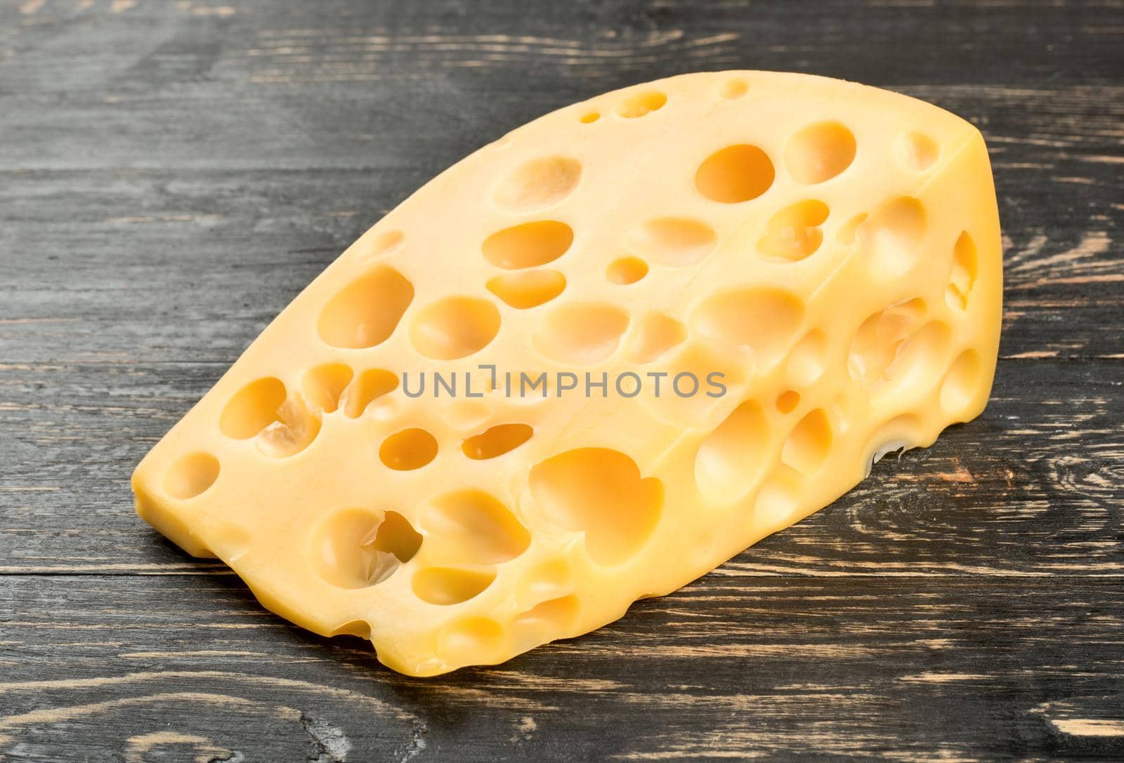 Piece of cheese with holes on dark table close up