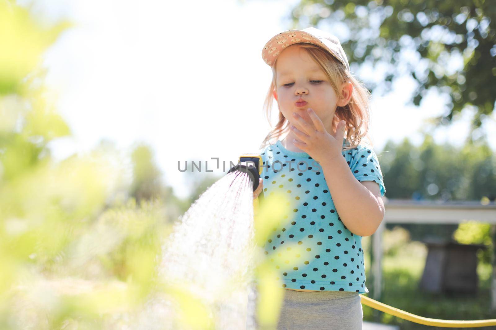 Adorable little girl playing with a garden hose on hot sunny summer day