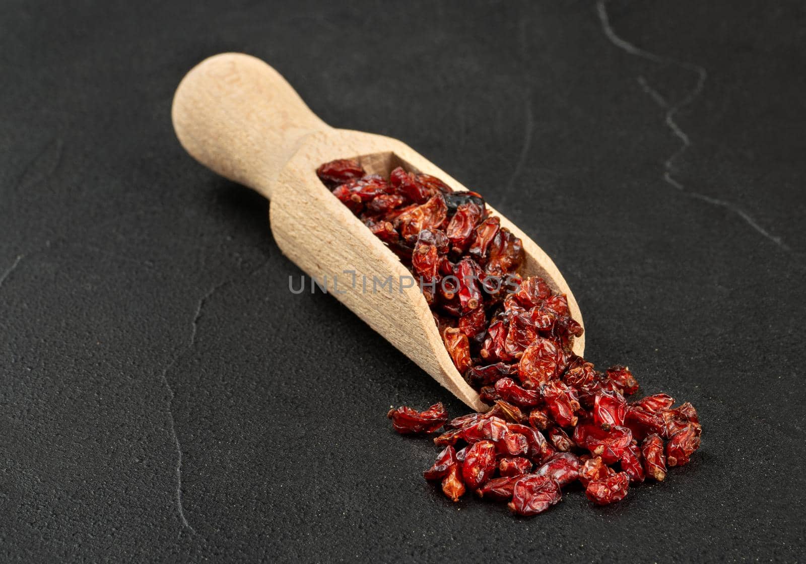 Dry barberry in a wooden scoop on a concrete background