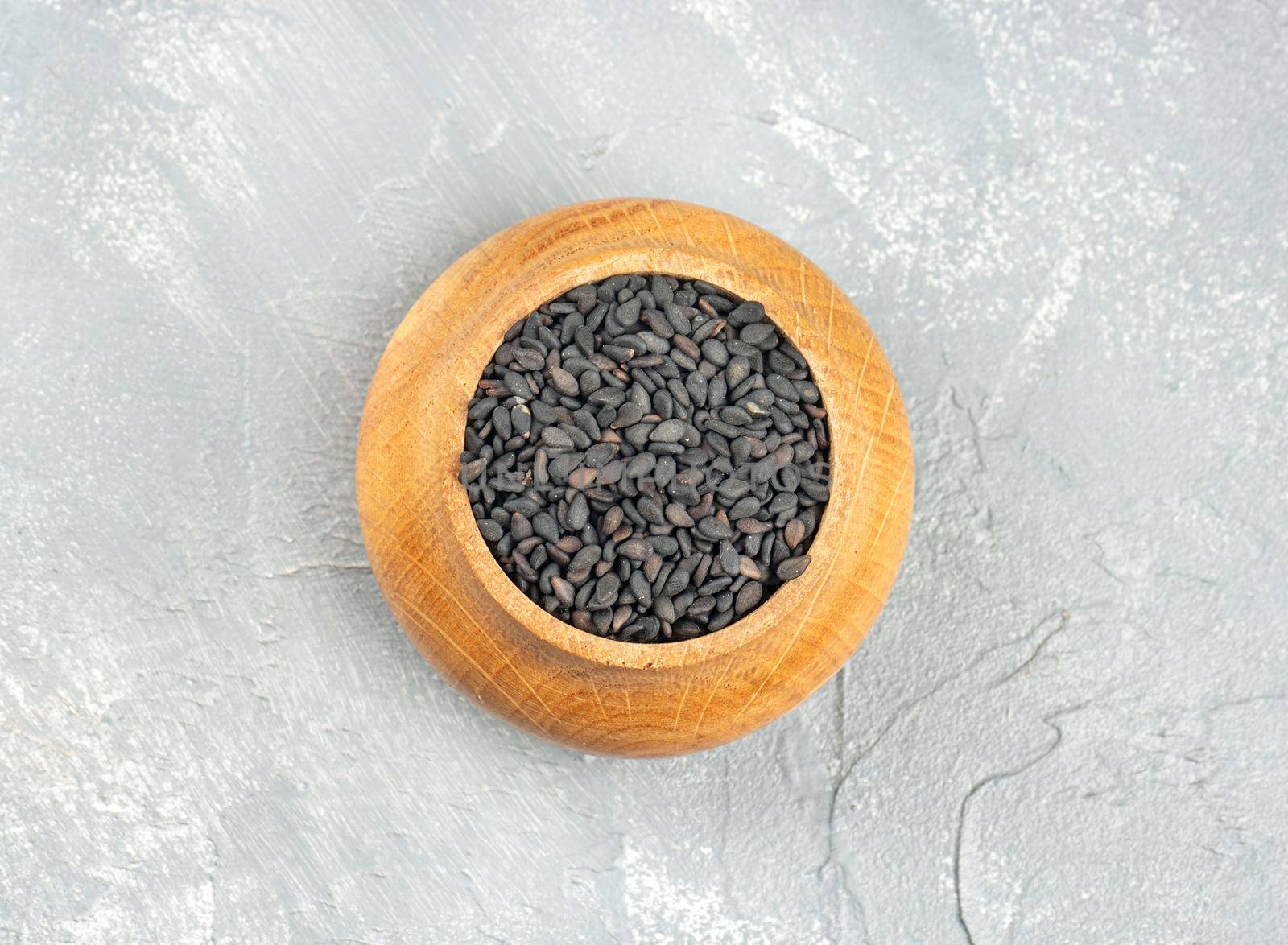 Black sesame in a wooden container on a light background, top view