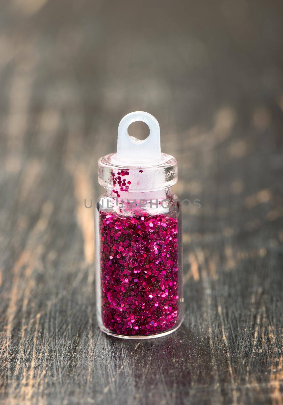 Bottle with purple sequins for the design of nails and makeup on a wooden background