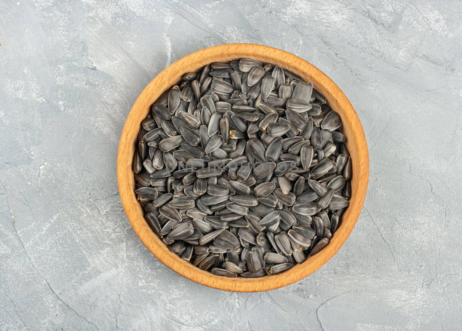 Large wooden bowl with sunflower seeds on concrete background, top view