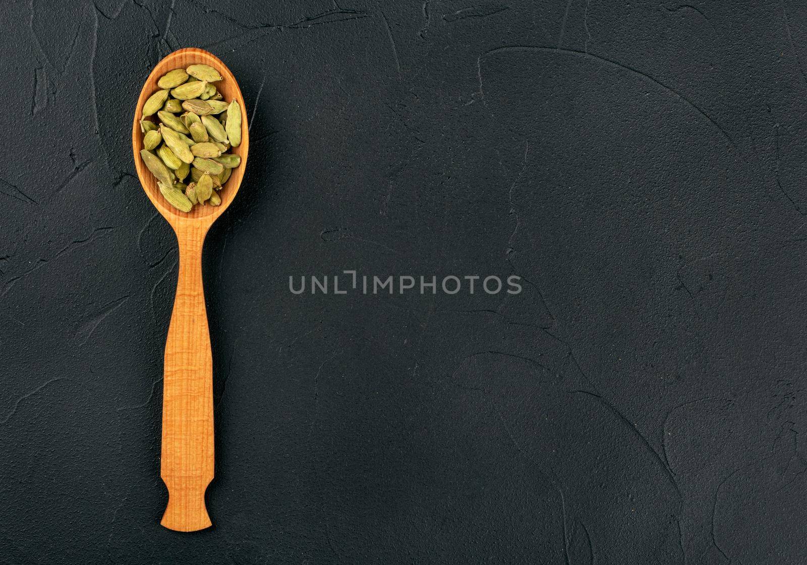 Green cardamom in wooden spoon on dark background, top view