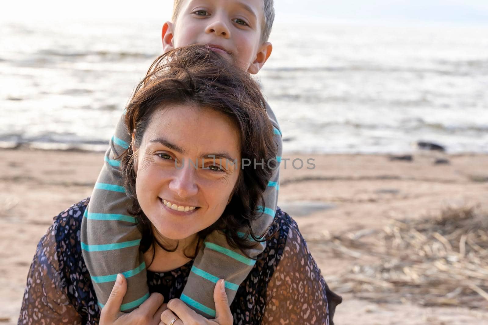 A cute happy preschooler boy hugs his mom on the seashore in the sunset rays. love for parents. Mother's Day