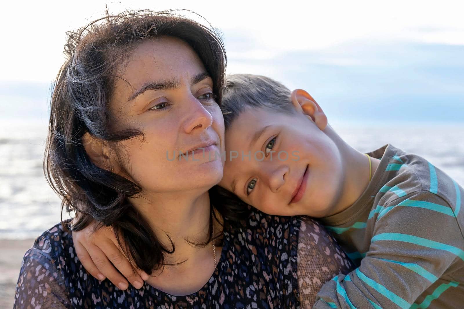 A cute happy preschooler boy hugs his mom on the seashore in the sunset rays. love for parents. Mother's Day