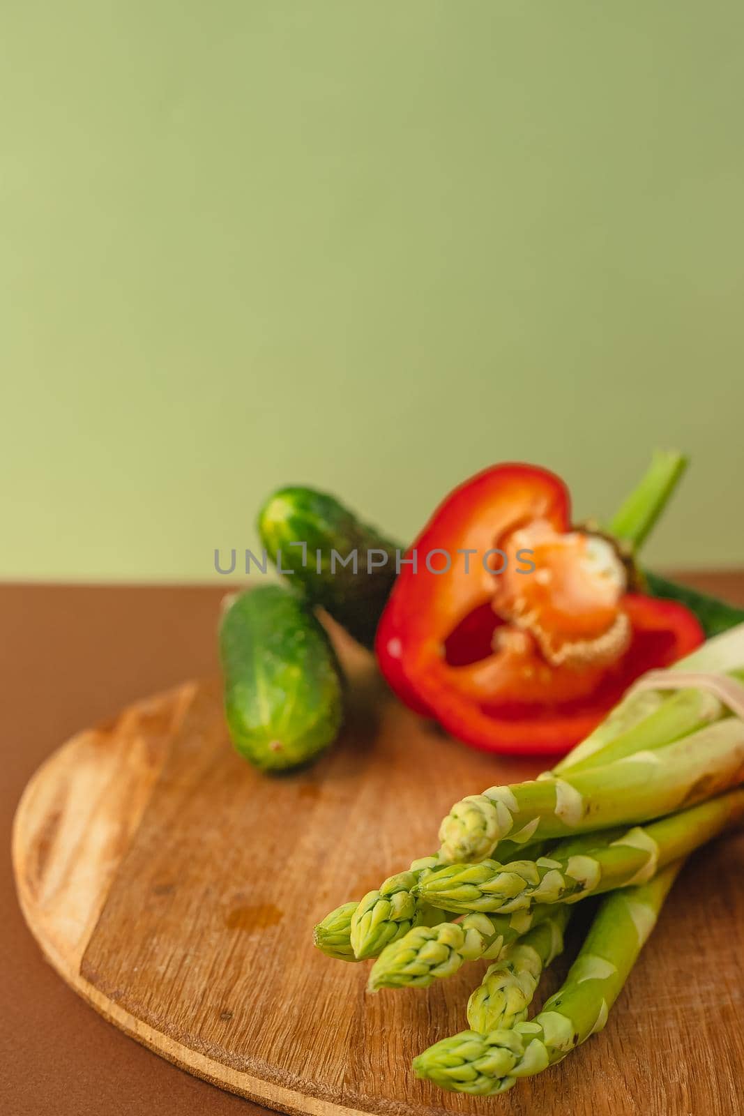 Vegetables lie on a wooden board: tomatoes, asparagus, cucumbers, red bell peppers. brown, light green background. place for text
