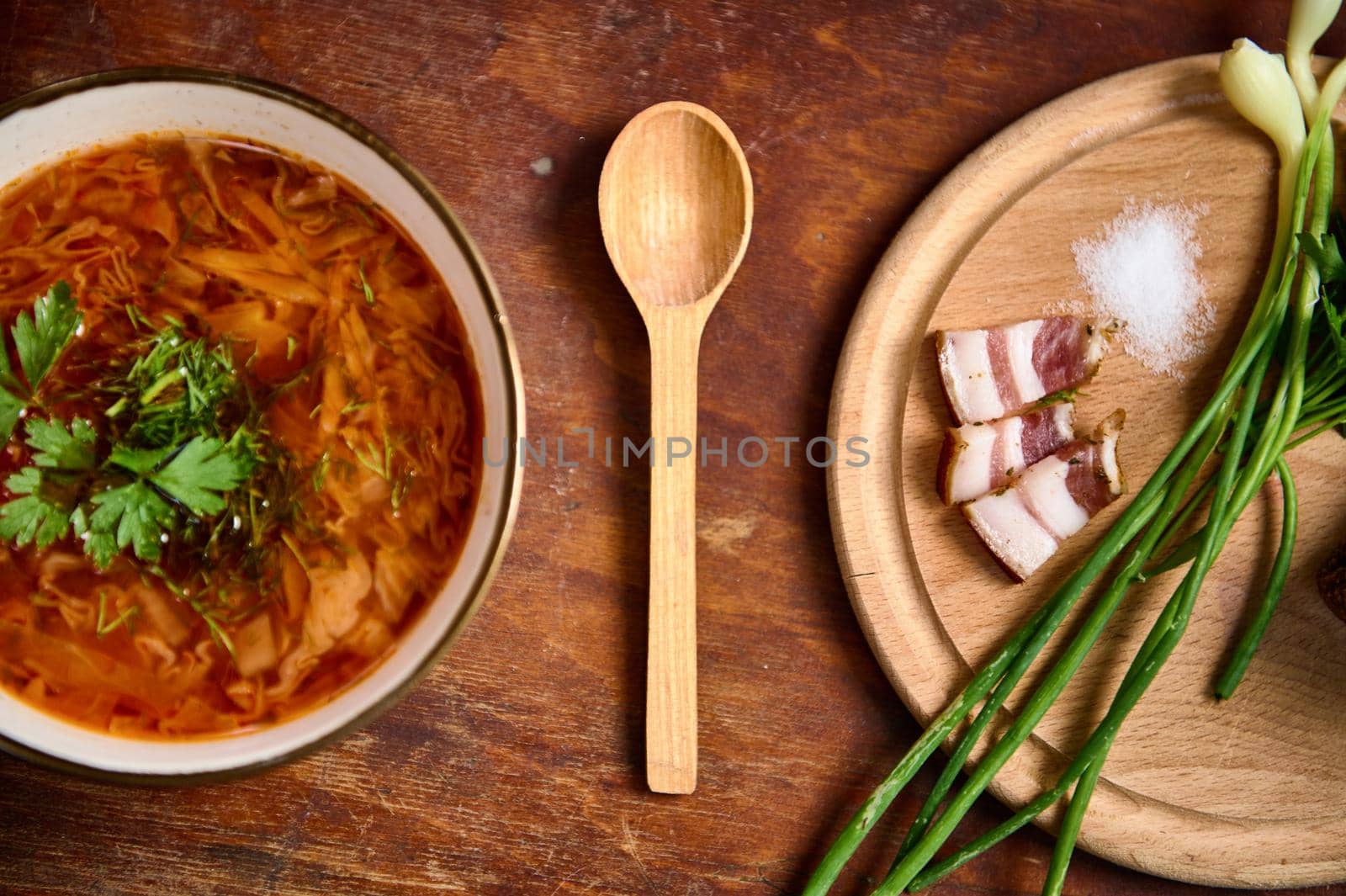 Served bowl with traditional Ukrainian Borscht, wooden board with sliced bacon, onion and salt on wood table background. by artgf
