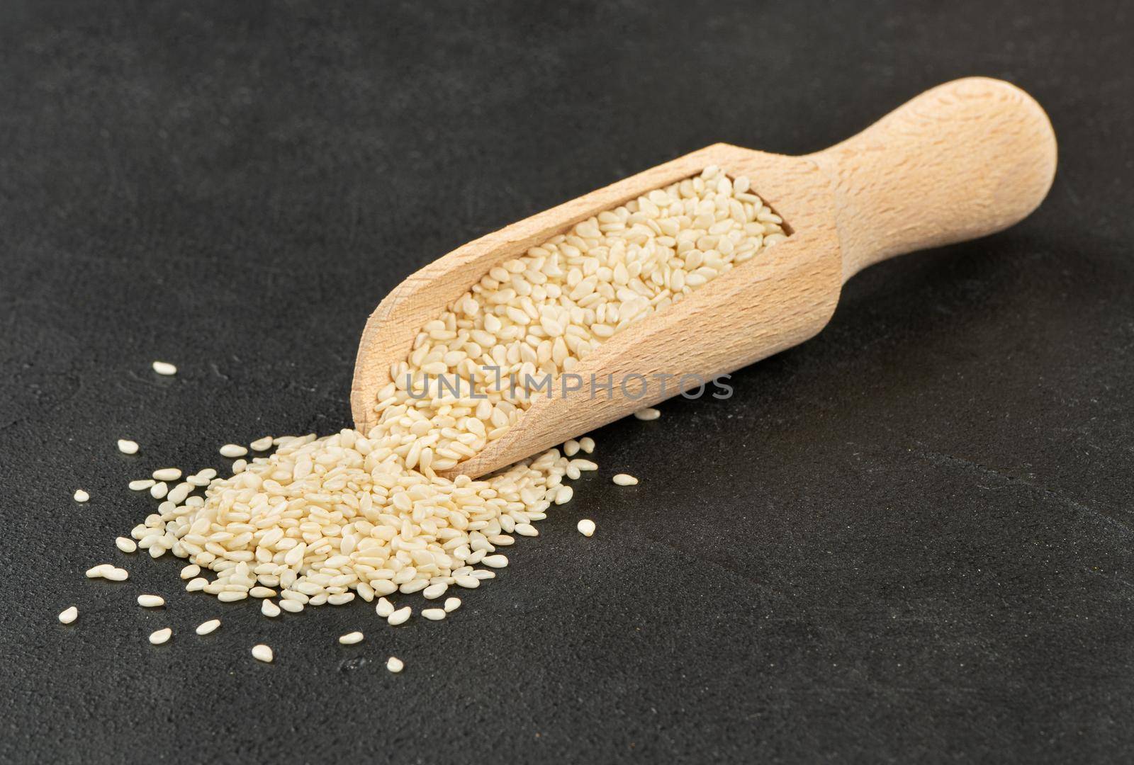 Sesame seeds in a wooden scoop on a concrete background