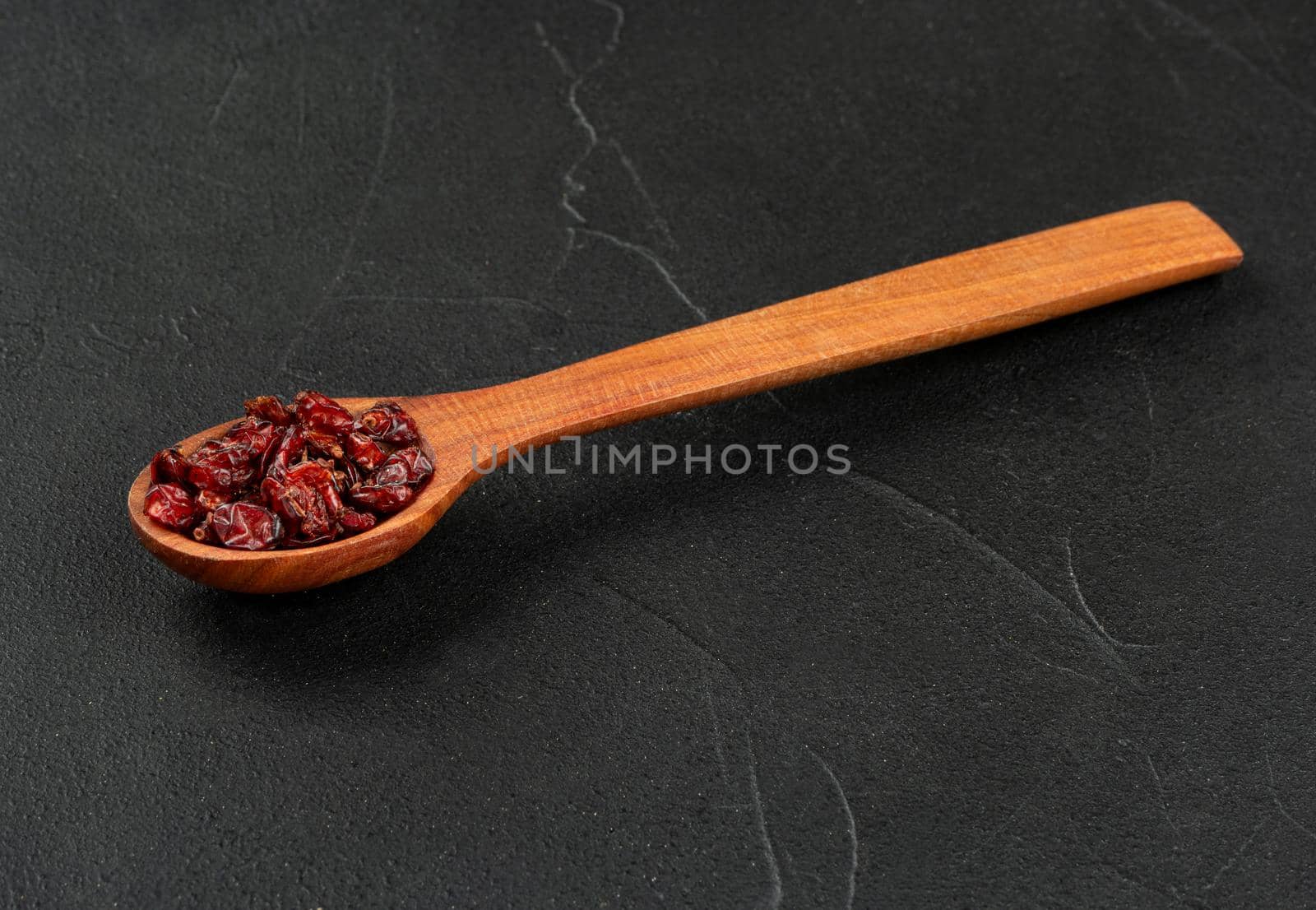 Small spoon with dry barberry on dark background