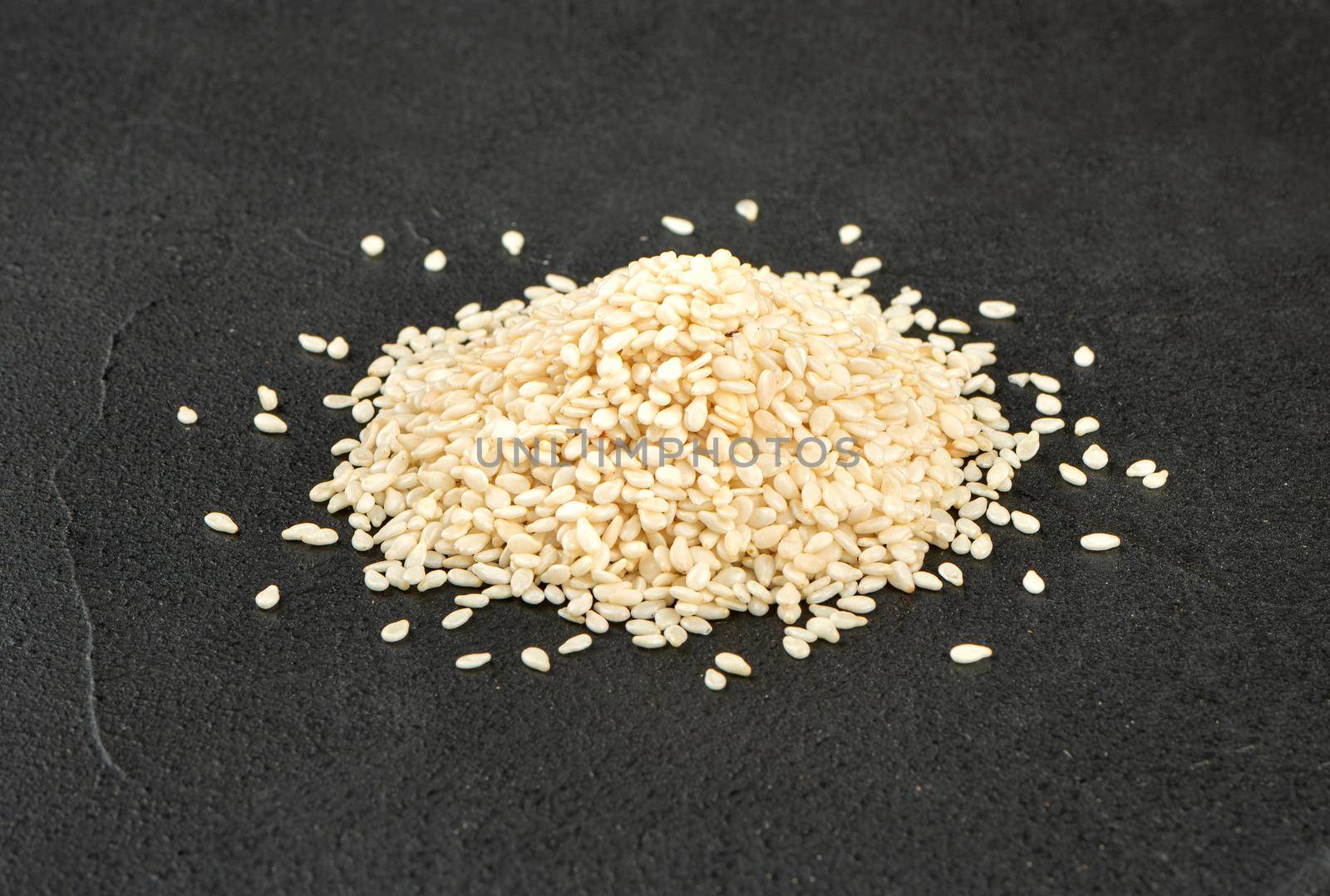 Pile of white sesame seeds on a dark concrete background