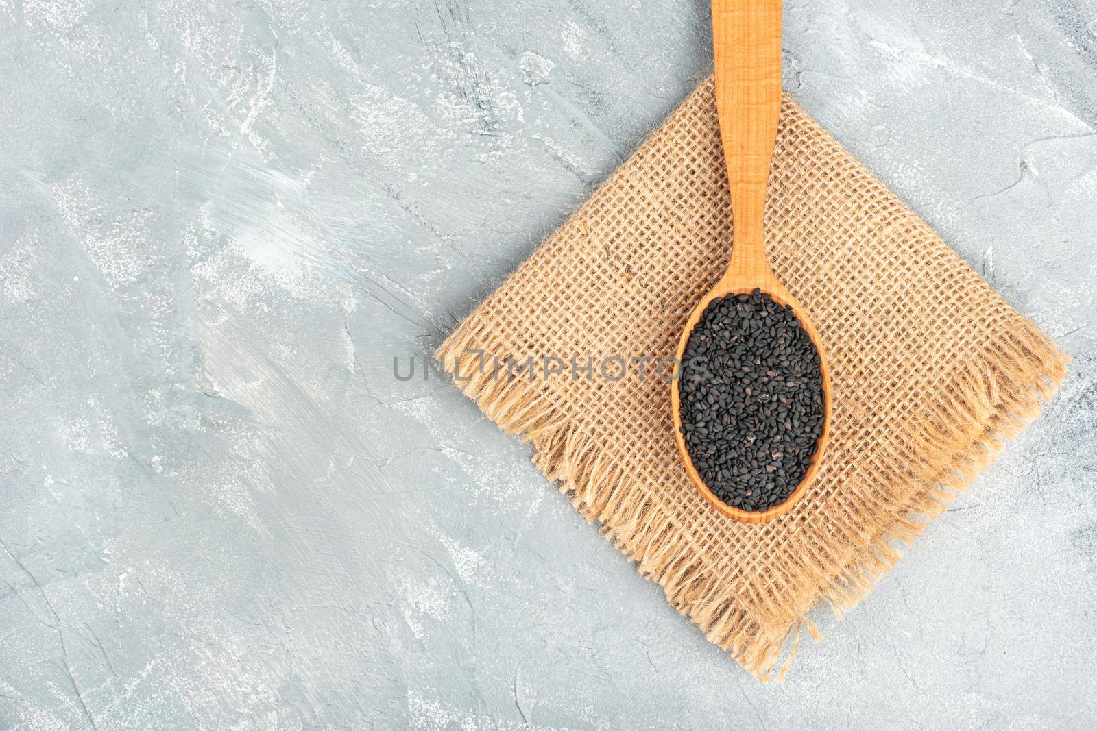 Black sesame in wooden spoon on burlap and light background