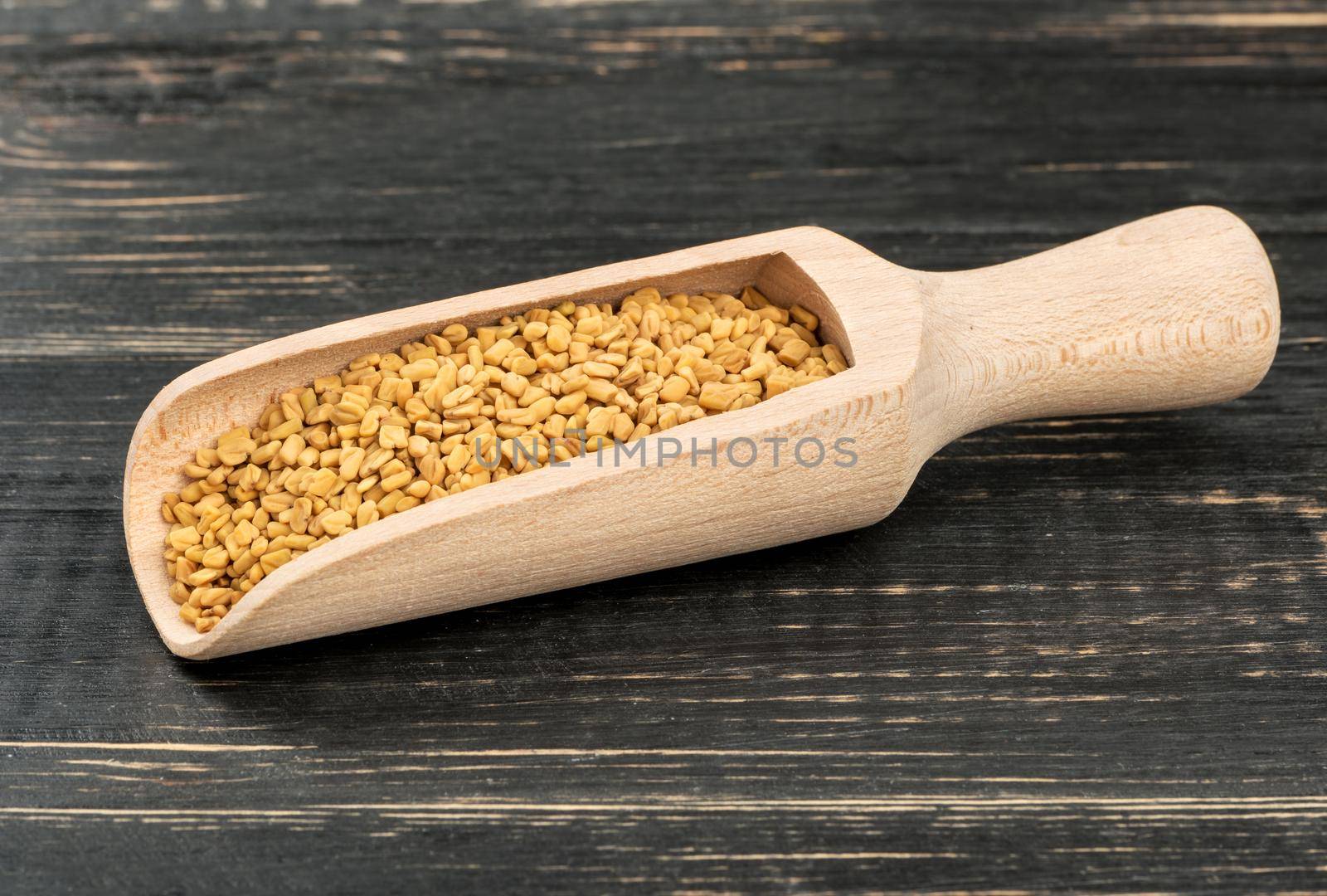 Fenugreek seeds in scoop on wooden background