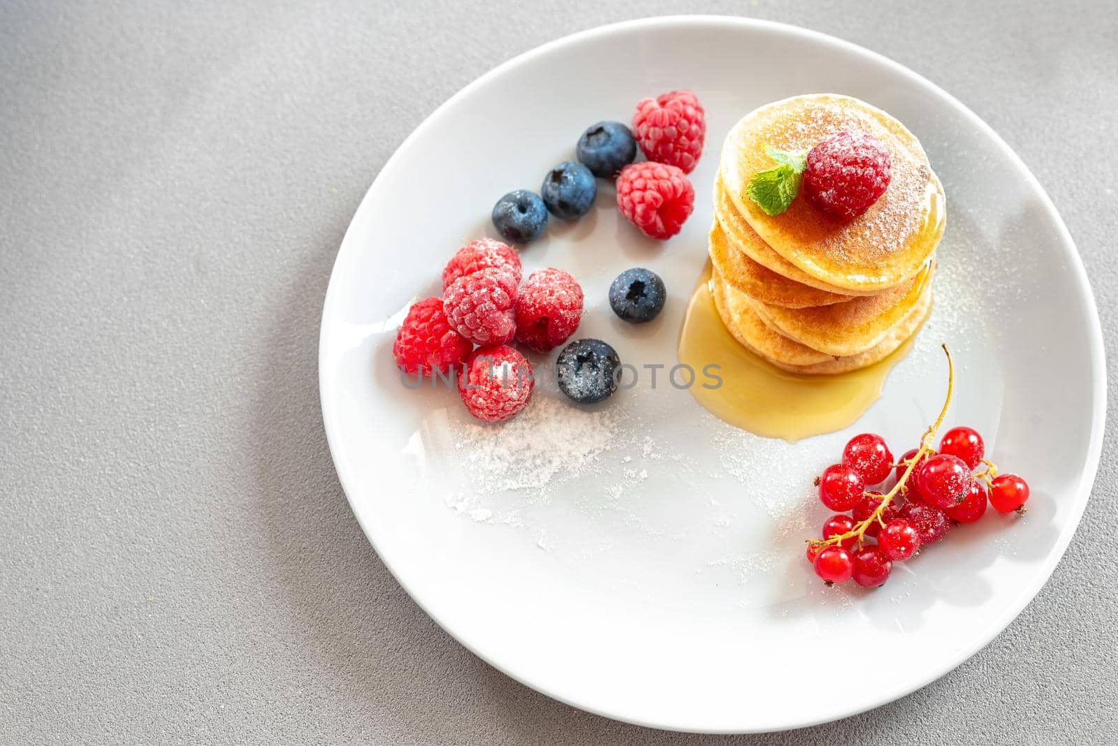 Pancakes on a white plate on a light background with berries and honey. empty space for text.