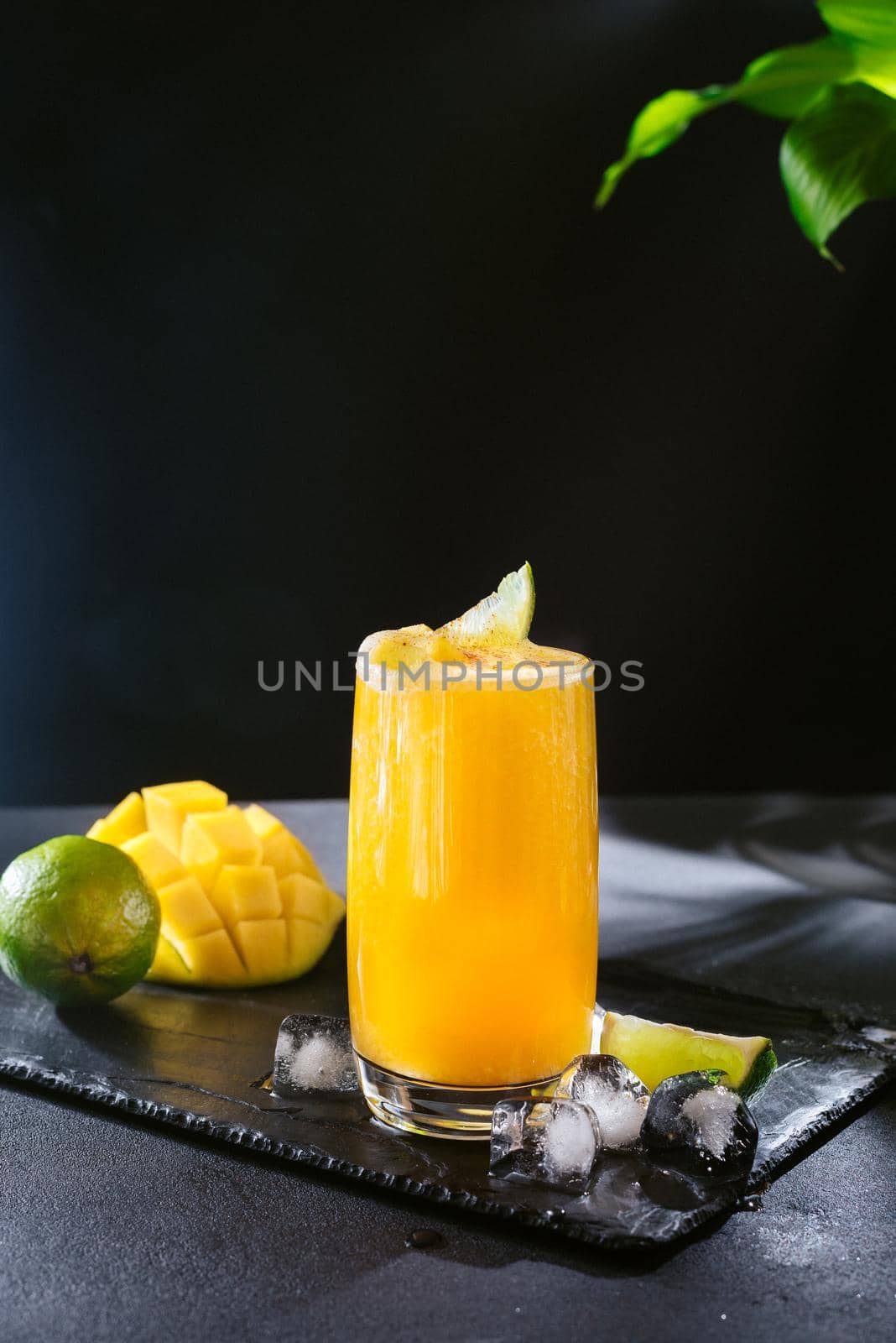 Bright yellow summer mango cocktail. Slices of mango and lime on a black background. Seasonal drink. Cocktail for vegetarians and those on a diet. Healthy Food.