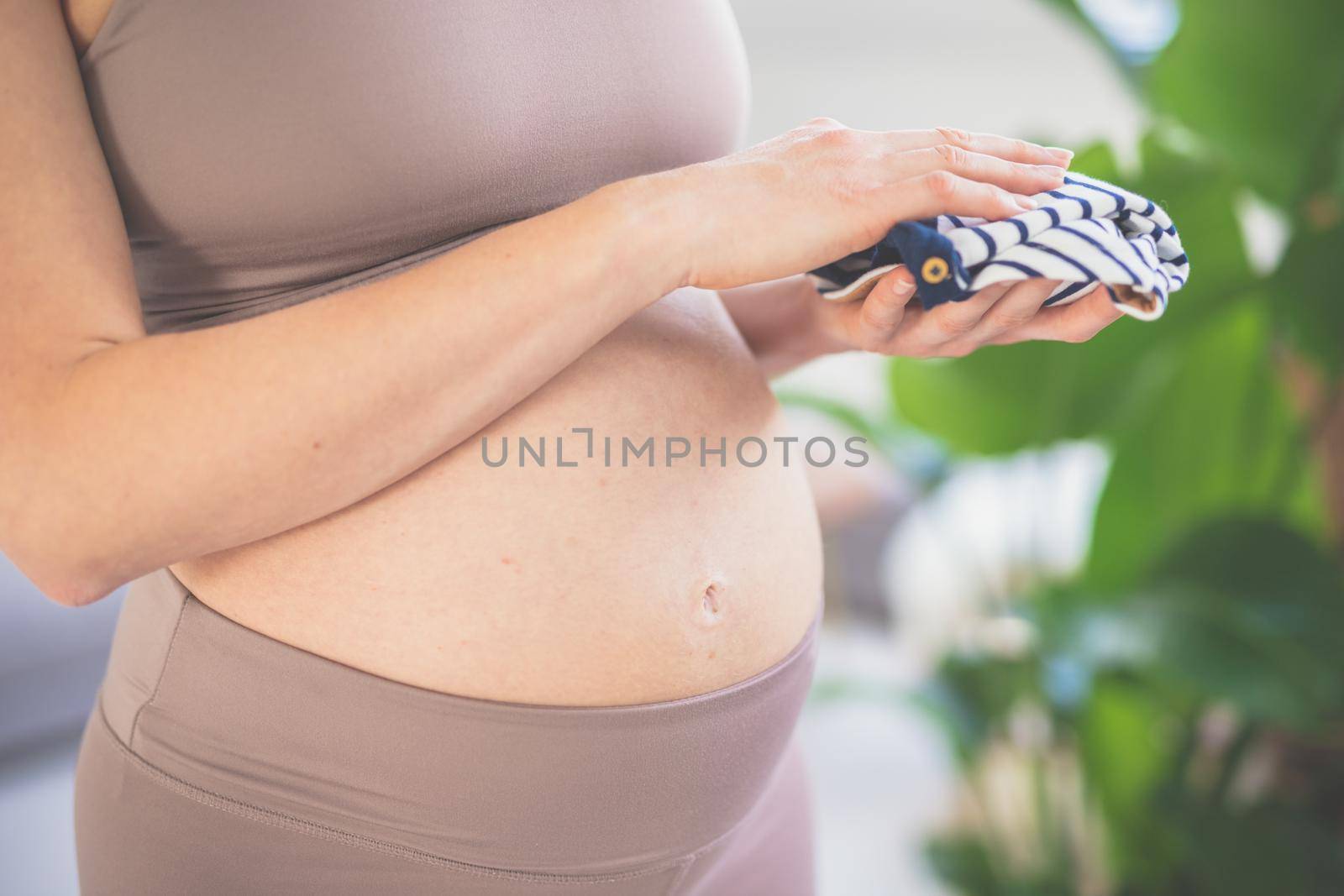 Pregnant woman ready for delivery, holding little clothes for newborn baby. Pregnant woman belly. Pregnancy Concept. Pregnant tummy close up.