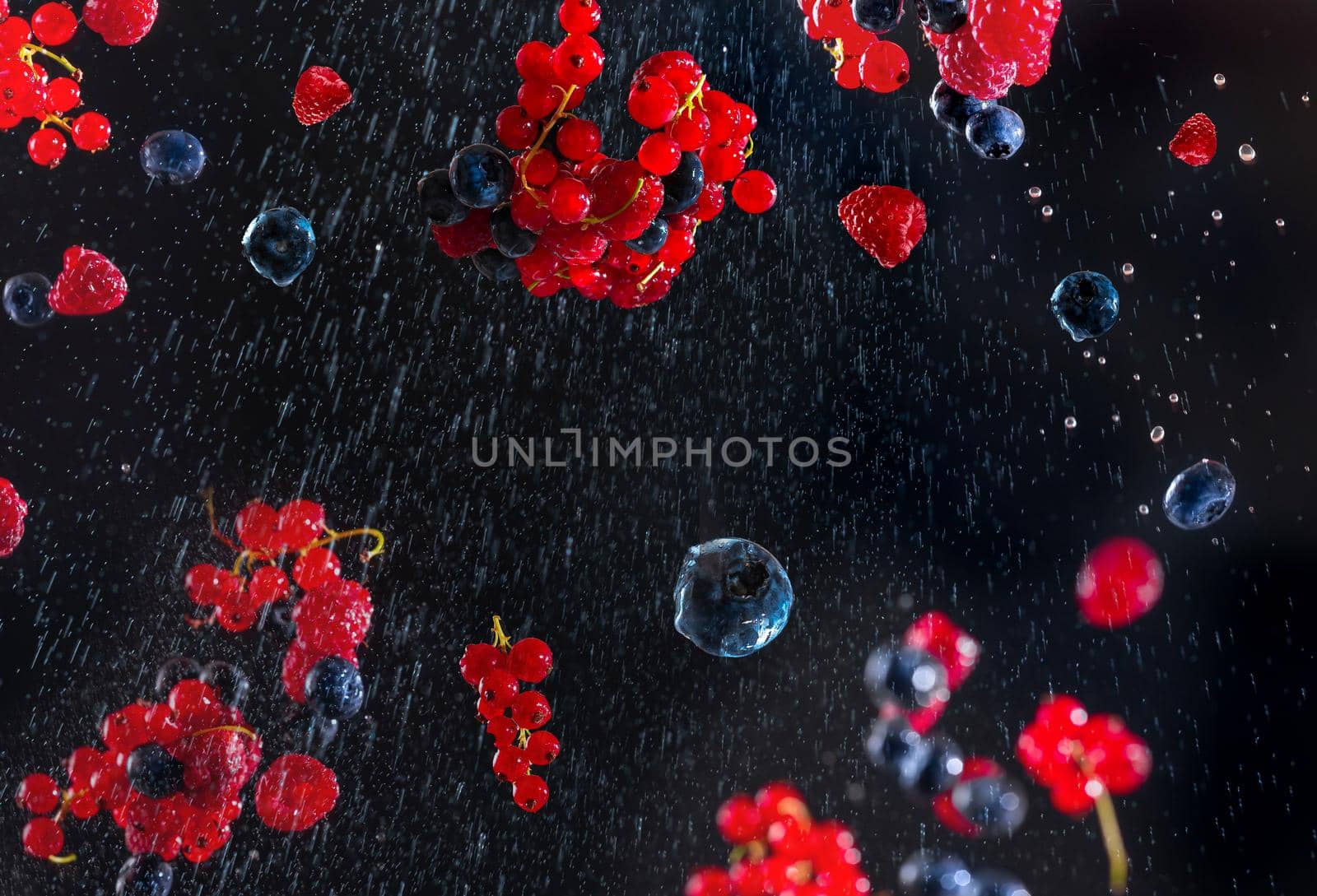 Fresh berries on a black blue background with water droplets flying in different directions. Many different berries in the form of a frame on a dark background by gulyaevstudio