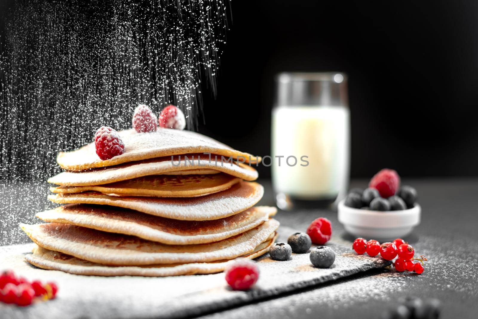 Large American pancakes on a dark background. Breakfast European. Chef sprinkles pancakes with powdered sugar on black background. Food for breakfast healthy eating. Pancakes with honey. Homemade pancakes on a white background. European breakfast pancakes and berries. Pancakes without butter with berries. Food for vegetarians and for dieting. American Pancakes Mini.