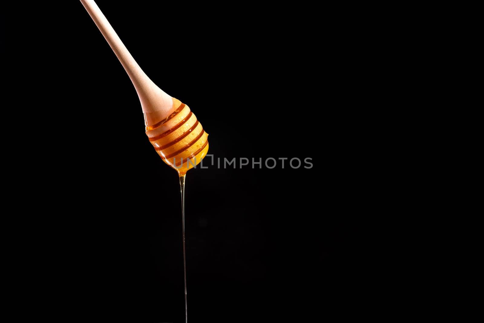 Shiny golden honey dripping off of a spoon into a wooden bowl with black background. Honey spoon on a black background. Blank space for text