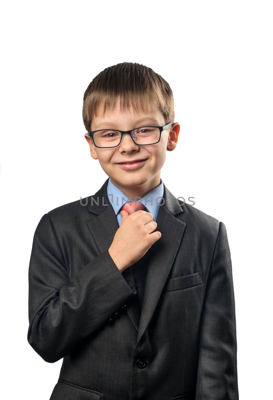 Smiling schoolboy straightens his tie against a white background