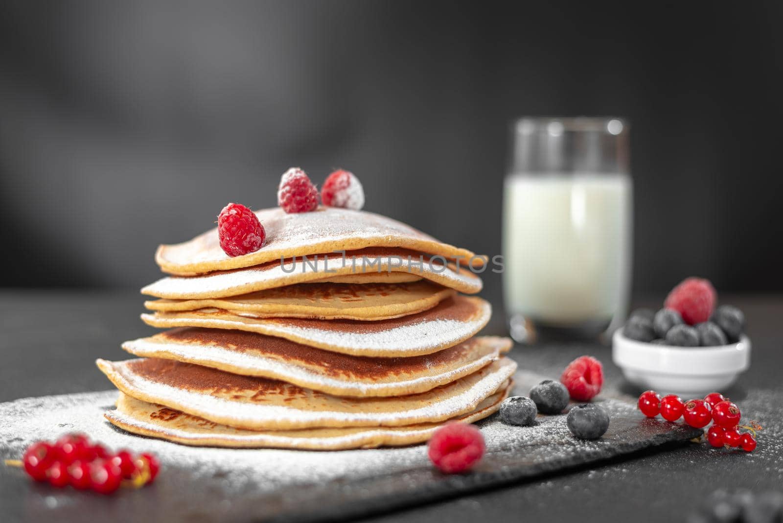 Serving pancakes with powdered sugar and berries. Chef man hand. Beautiful food still life. Natural light, slightly toned image, dark black background with text area. Horizontal view