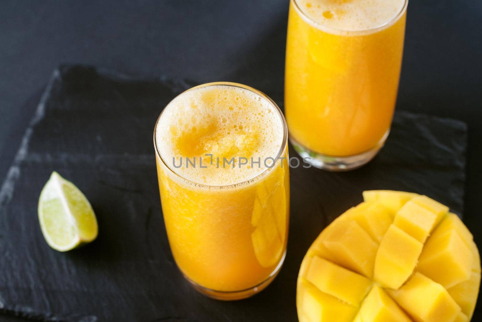 Mango juice on a dark background. Summer drink with ice and slices of mango and lime. Mango and lime juice nectar. A refreshing summer drink on a black background. Bright yellow and black colors