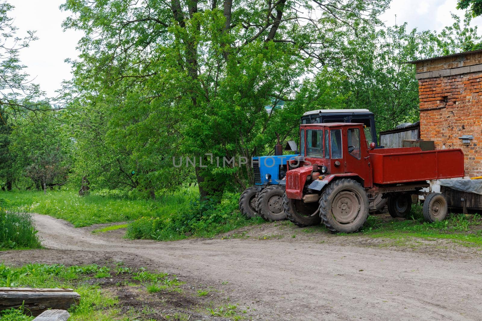 two old blue and red soviet tractors near brick building in summer day apple garden
