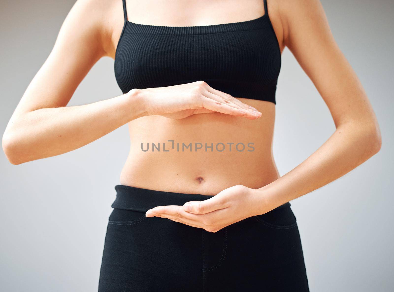 Building that mind gut connection. Shot of a woman forming a circle with her hands in front of her belly. by YuriArcurs