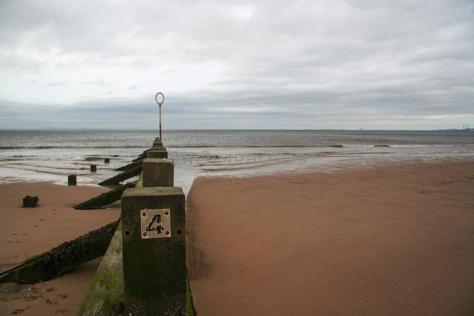 Old wooden groyne, with number 4 on it, overcast day, sea in background. Portobello beach, Edinburgh.
