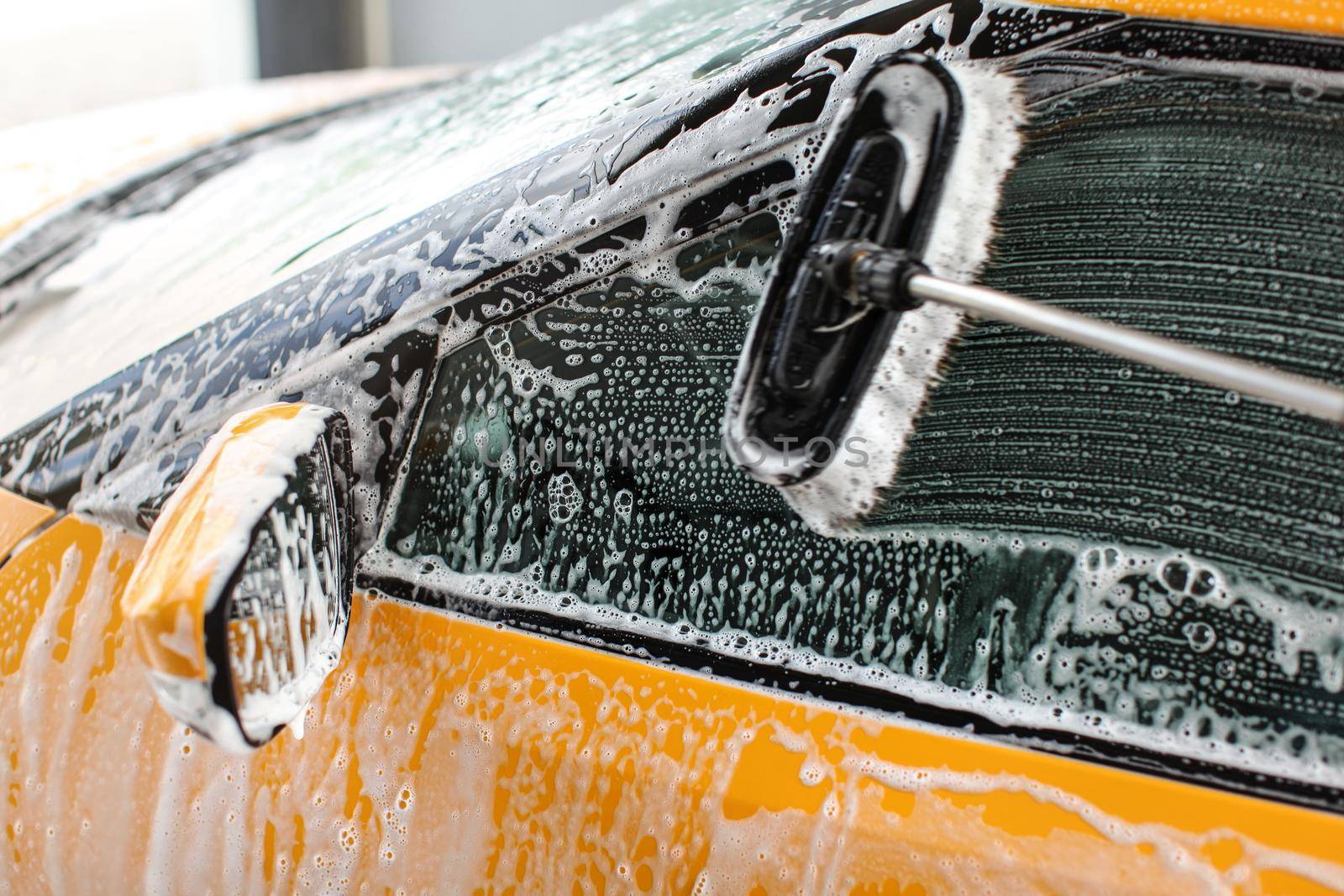 Side window of yellow car washed in self service carwash, brush leaving strokes on glass covered with shampoo foam.