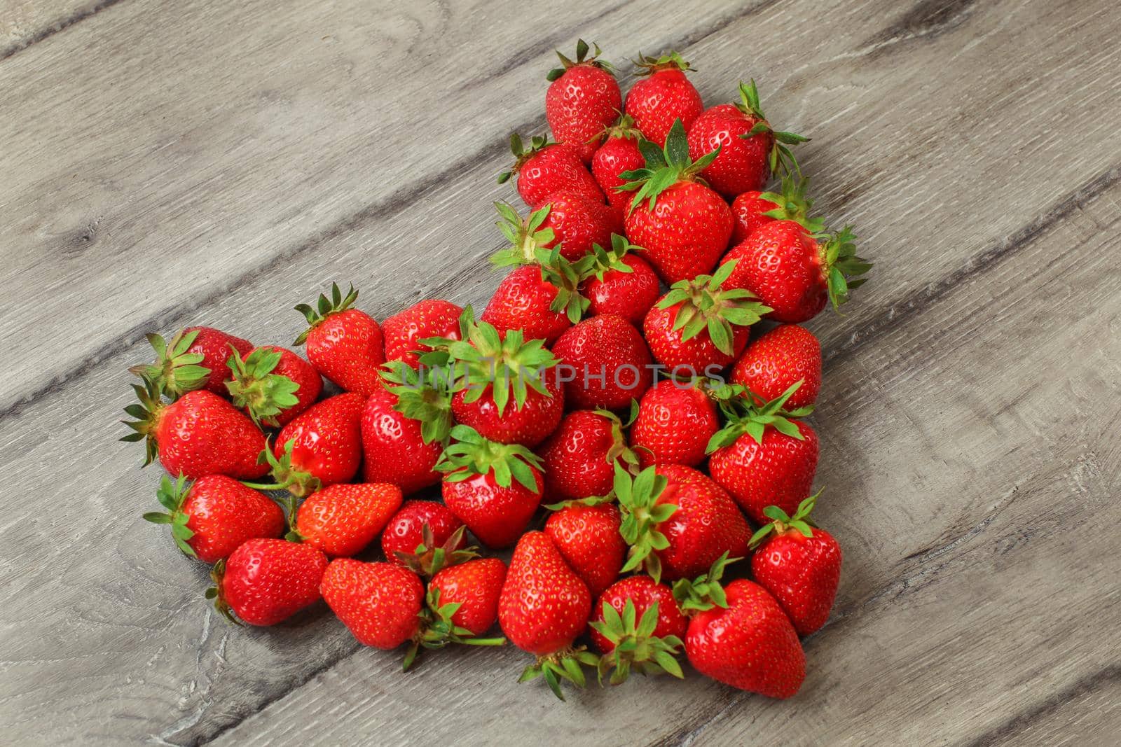 Strawberries arranged in shape of heart, placed on grey wood desk.