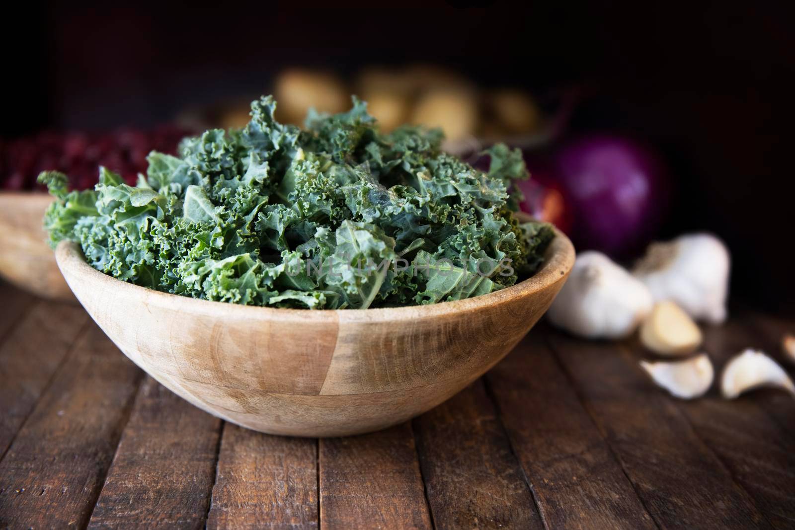 Fresh chopped kale in wooden bowls with garlic and other ingredients in the background