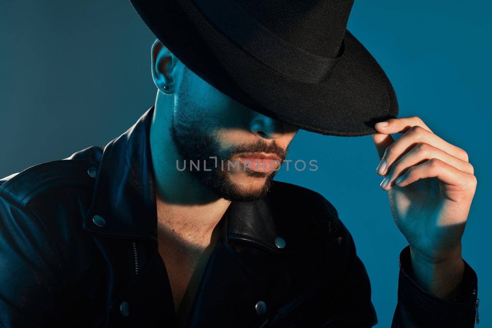 A hat completes the look. Conceptual shot of a stylish young man posing in studio against a blue background. by YuriArcurs