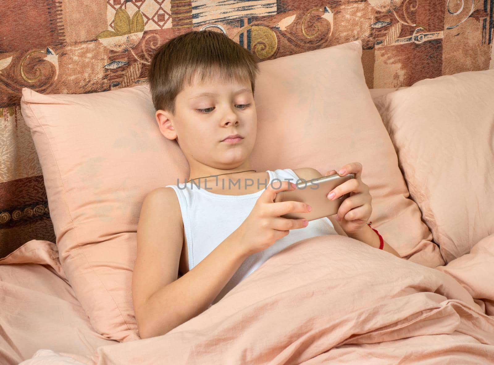 Young boy plays games on phone in bed