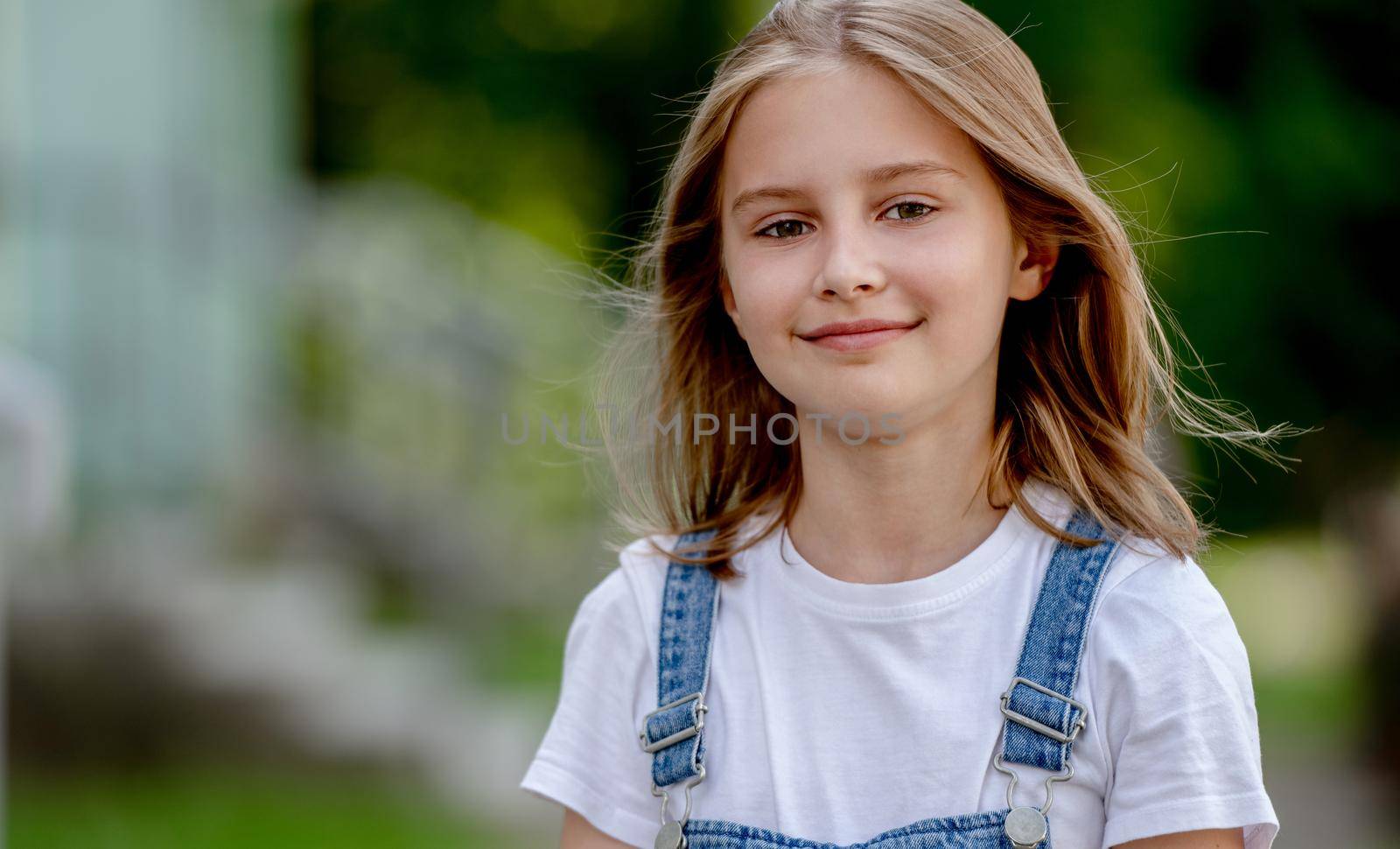 Beautiful preteen girl in city in summertime closeup portrait. Pretty female kid looking at camera in sunny day with blurred background