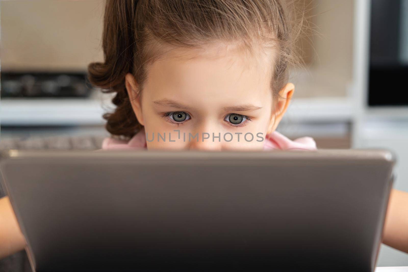 A close up of a little girl looking at a laptop or tablet with copy space by Mariakray