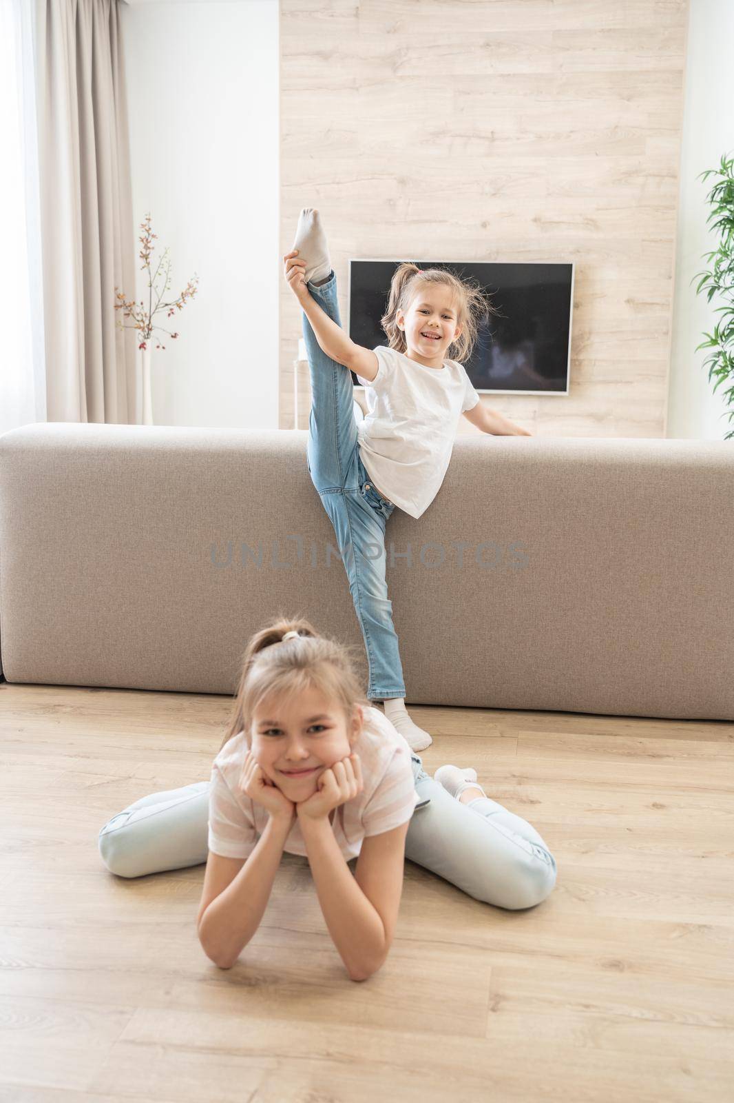 Two girls doing stretching exercises in living room at home. Friendly sisters concept by Mariakray