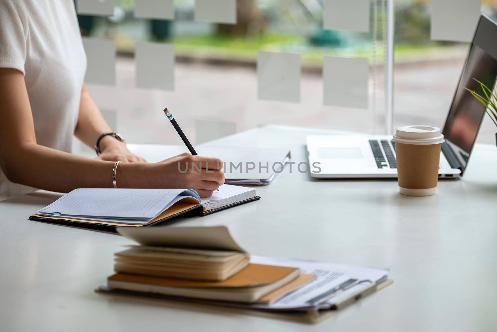 Close up asian female is taking notes on her notebook for online classes, study ideas and note-taking.