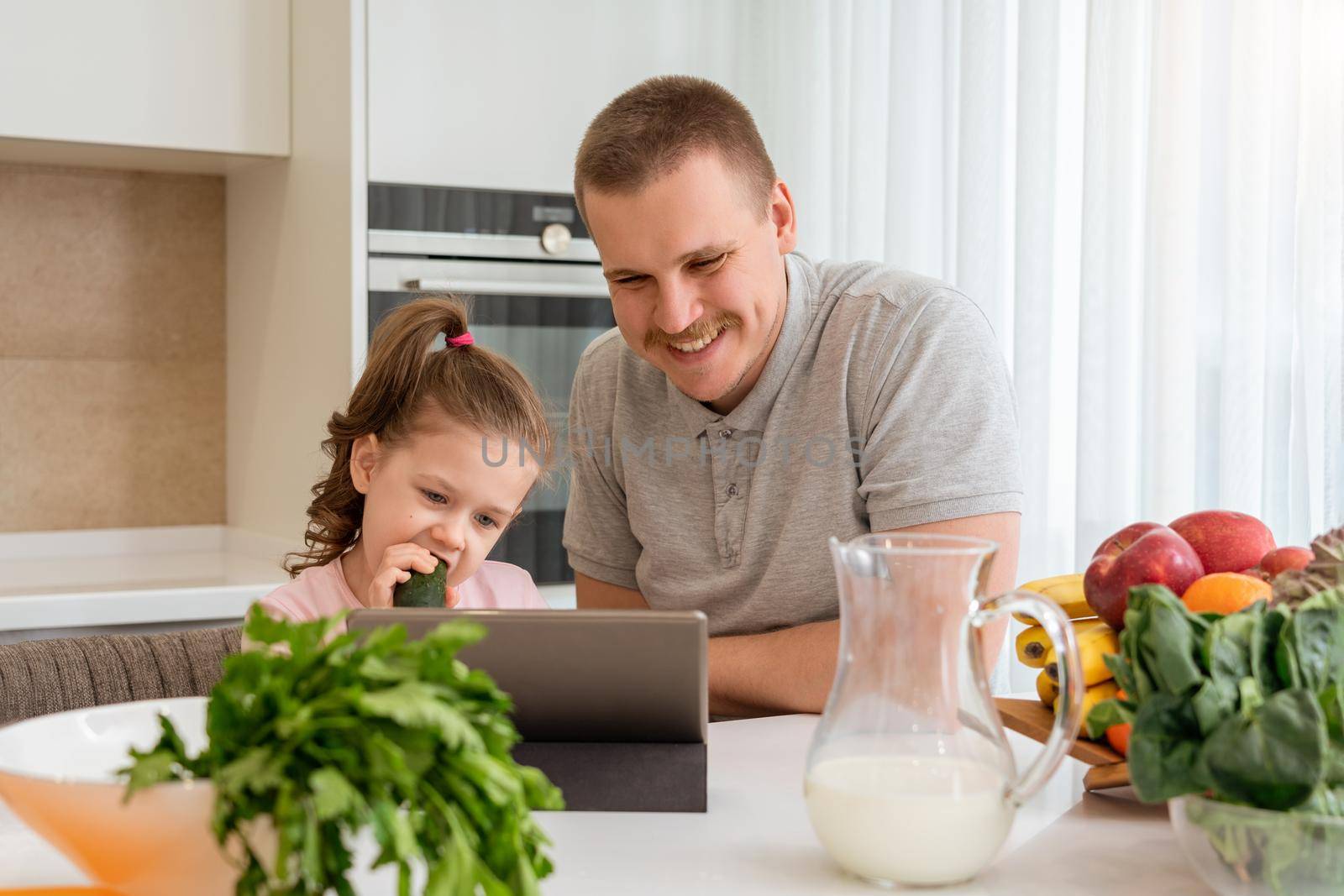 Father And Daughter Using Digital Tablet In Kitchen At Home by Mariakray