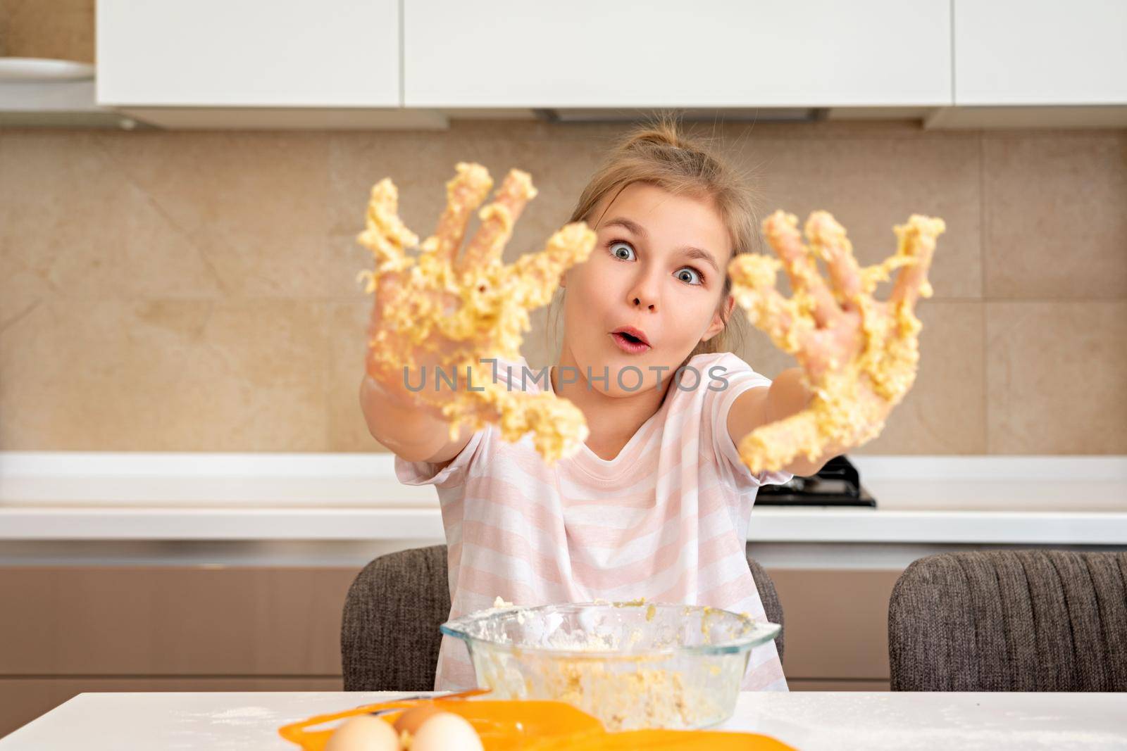 Teenage girl shows dirty hands in dough having fun in kitchen by Mariakray