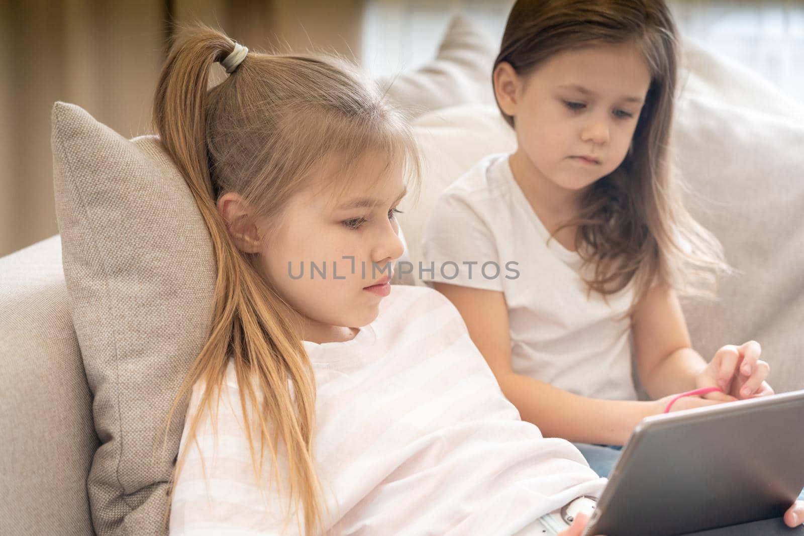 Two little sisters Lying On Couch And Using Tablet