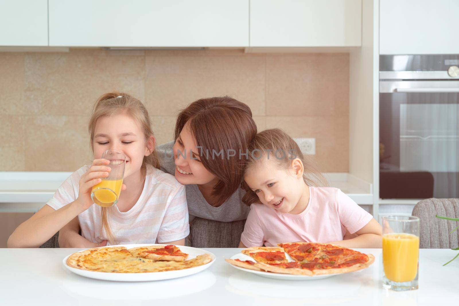 Mother and two daughters eating homemade pizza at a table in kitchen