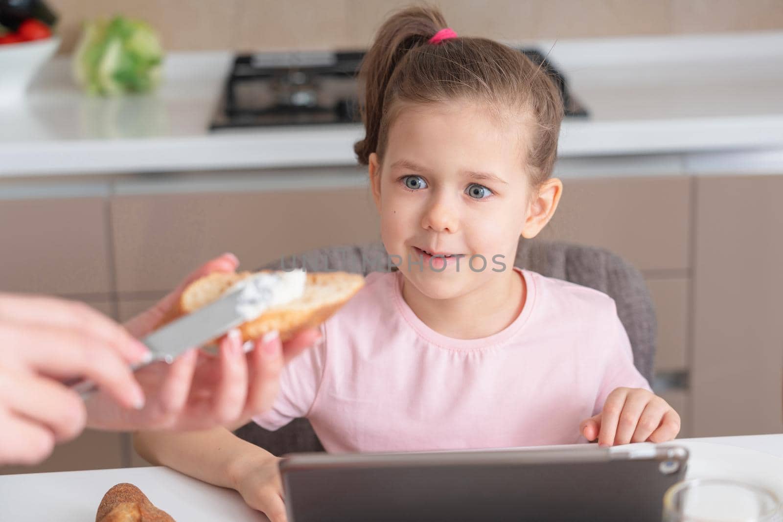 Young woman feeding her daughter with appetizing homemade sandwich for breakfast