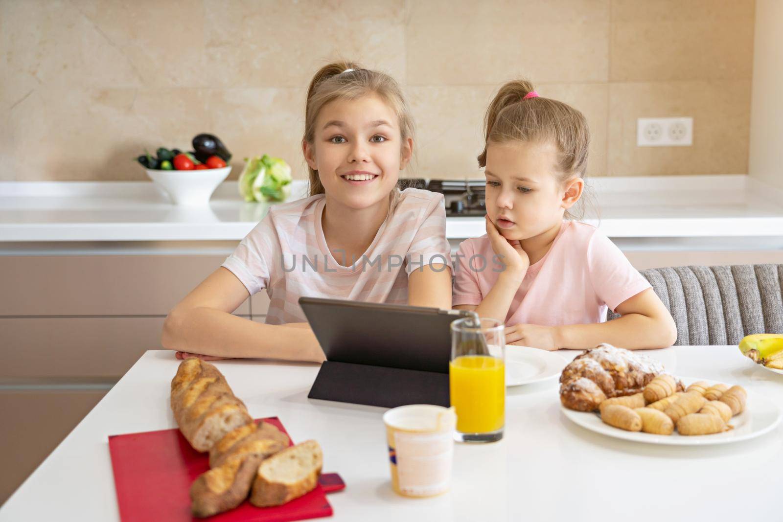 Two sisters having breakfast and watching cartoons on tablet together, happy family concept by Mariakray