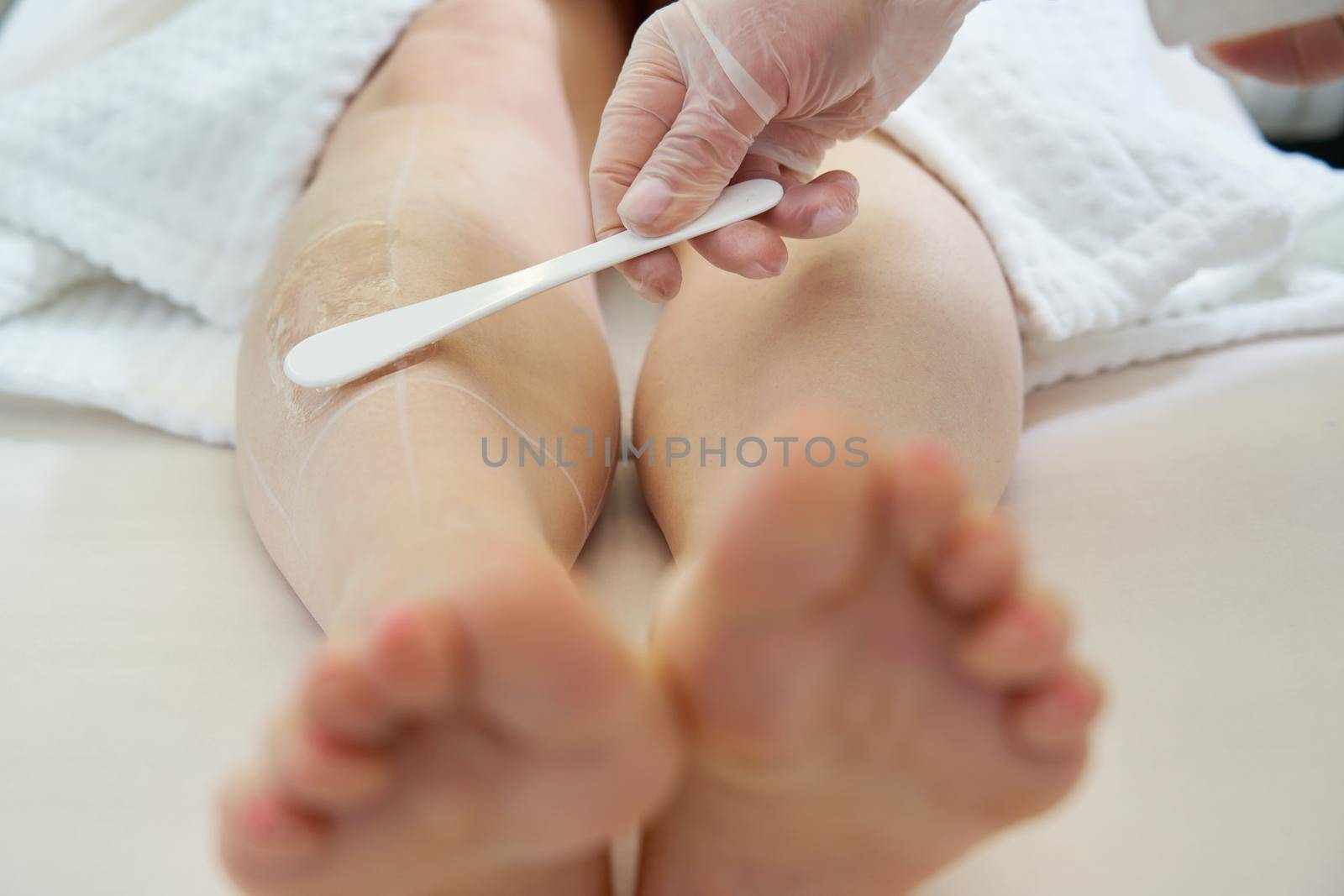 Cosmetologist preparing female patient for laser hair removal on legs in spa salon by Mariakray