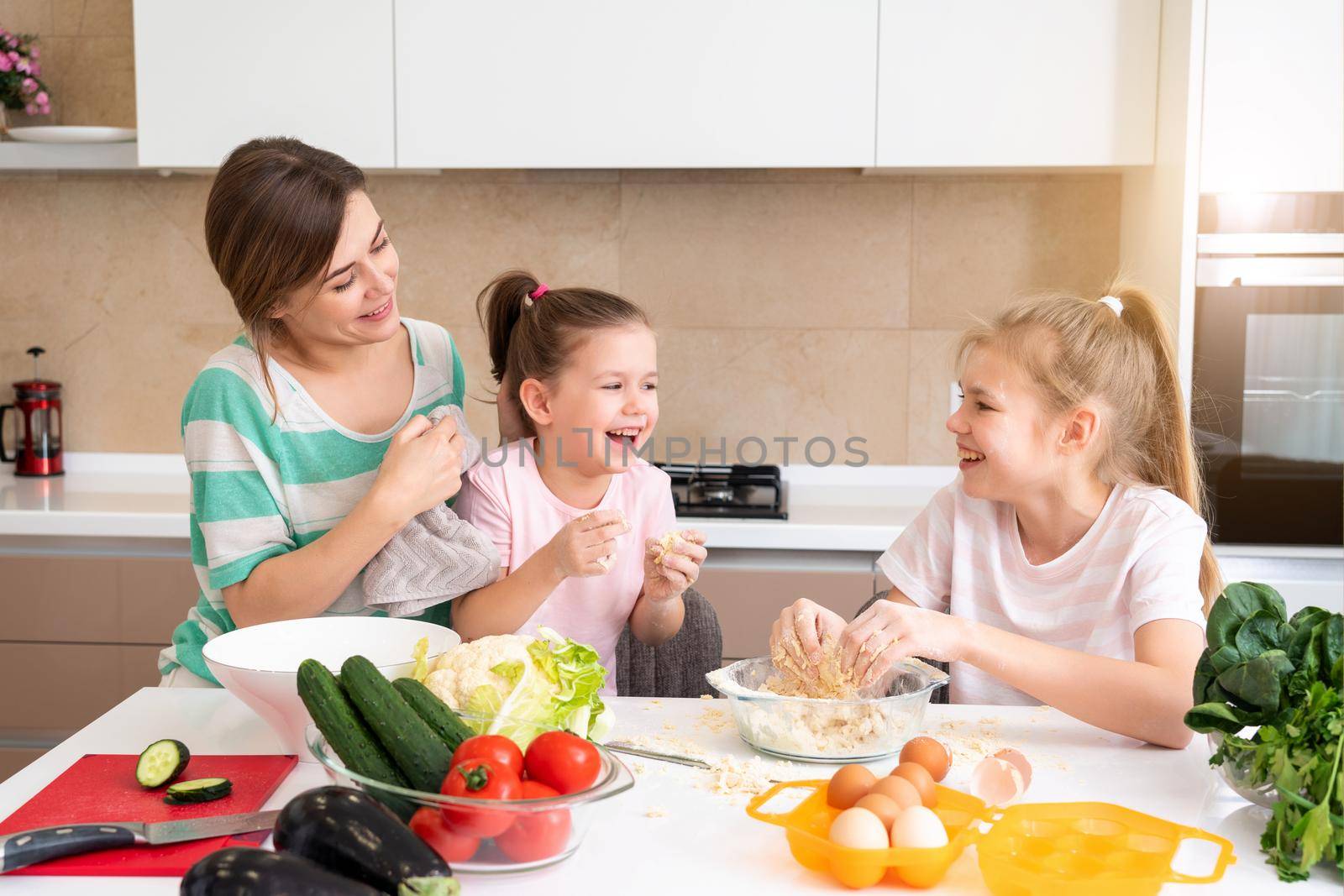 Mother and two daughters making dough in the kitchen and having fun, happy family and single mother concept by Mariakray